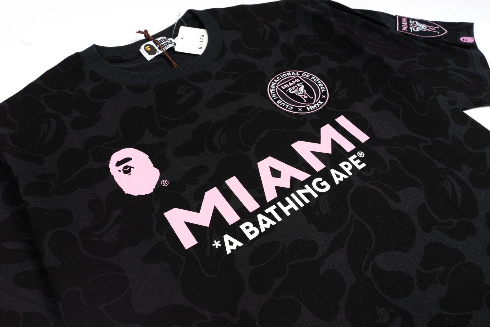 Camiseta BAPE x Inter Miami CF Camo Masculina em preto, feita com 100% algodão, decote redondo e mangas curtas. Apresenta estampa do macaco BAPE e logo do Inter Miami na frente, com as letras 'BAPE' e o número '93' representando o ano de fundação da marca japonesa nas costas.