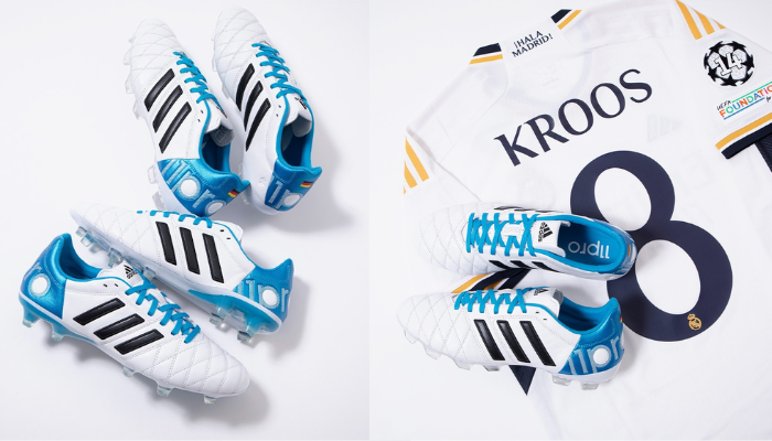 chuteira de futebol Adidas 11Pro FG Elite Kroos Remake na cor branca, com detalhes em azul e preto. O cabedal em couro Taurus e a costura de vampiro são evidentes, assim como a marca Adidas nas laterais. A sola moderna Copa Pure pode ser vista na parte inferior da chuteira.