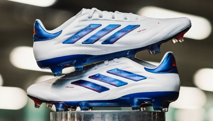 chuteira Adidas Copa Pure 2+ FG Advancement na cor branca com detalhes em azul e vermelho. A chuteira é feita de couro de bezerro premium e possui um ajuste anatômico graças ao Primeknit. A tecnologia FusionSkin proporciona um toque macio na bola, e o solado TorsionFrame oferece tração e suporte em campos de grama natural.