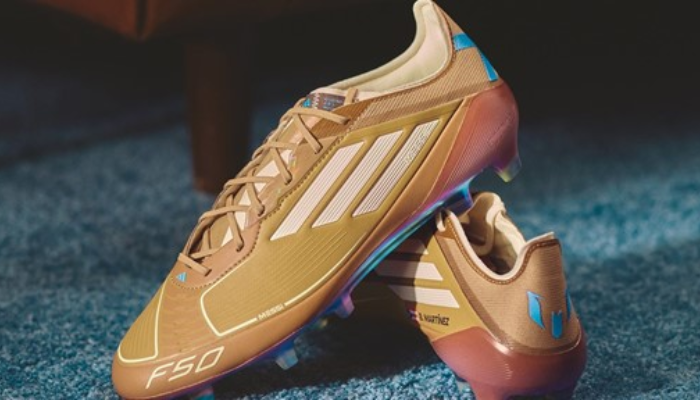 Chuteira Adidas F50 Elite FG Messi x Bad Bunny em dourado, azul e branco. Chuteira projetada para alta velocidade com tecnologia SprintWeb 3D para melhor controle de bola, PrimeKnit para ajuste moldado ao pé, e sistema de travas FG. Uma combinação de estilo, velocidade e liberdade em campo.