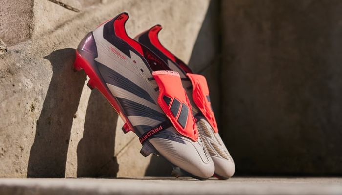 Chuteira Adidas Predator 24 Foldover Tongue FG, nas cores bege, preta e vermelha, celebrando 30 anos da linha Predator. Construída com materiais sintéticos reciclados, tecnologia HybridTouch 2.0 para conforto e ajuste moldado, além de StrikeSkin para controle da bola.