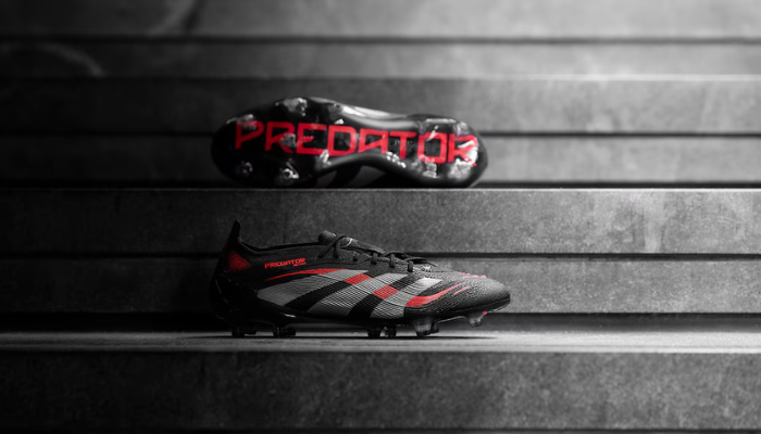 Chuteira adidas Predator 25 Lowcut FG Stealth Victory 2025 nas cores preto, cinza e vermelho. Modelo para gramado firme (FG) com cabedal HybridTouch e aletas de borracha Strikeskin para controle e precisão. Solado ControlFrame 2.0 para tração e estabilidade. Design com as 3 listras da adidas em ambos os lados, usada por Jude Bellingham e Gabriel Jesus.