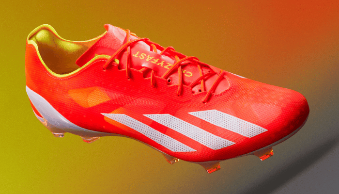 chuteira de campo adidas X Crazyfast+ FG Energy Citrus. A chuteira possui um cabedal vermelho vibrante (Solar Red) com listras e suporte do calcanhar brancos (Cloud White). Detalhes em amarelo neon (Solar Yellow) aparecem no interior do calçado e na placa da sola. O texto "adidas" está estampado na lateral da chuteira.