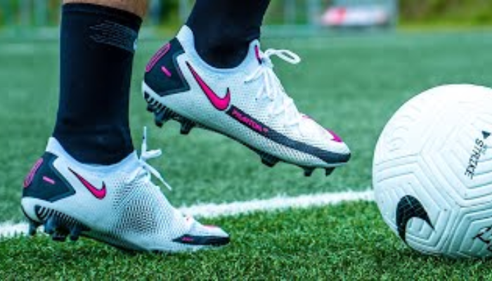 Chuteira de futebol Nike Phantom GT Elite Dynamic Fit FG em close, exibindo o design inovador com textura aderente na parte superior Flyknit, cor predominantemente branca com detalhes em preto e rosa, destacando a sola com tração especializada para melhor controle e agilidade em campo.