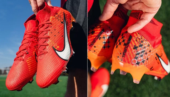 chuteira Nike Mercurial Dream Speed Superfly 9 Elite FG em um close-up. A chuteira é predominantemente vermelha com detalhes em laranja vibrante, preto e branco. O texto "Mercurial" e o swoosh da Nike estão visíveis na lateral