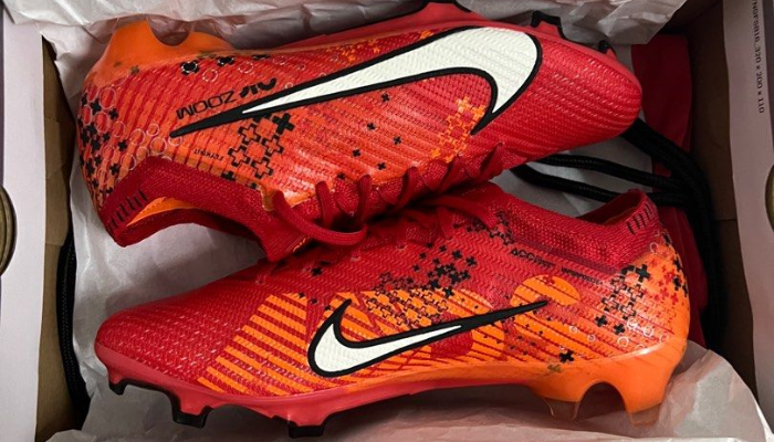 chuteira de futebol Nike Mercurial Dream Speed Vapor 15 Elite FG MDS 007. A chuteira possui um design predominantemente vermelho com detalhes em laranja vibrante, preto e branco. O cabedal é feito de material Vaporposite+ texturizado para melhor controle de bola. A chuteira possui um Flyknit envolvente para ajuste confortável e seguro.