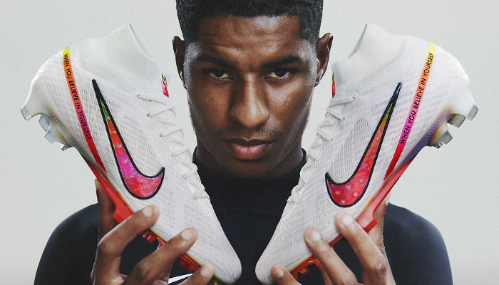  Chuteira Nike Air Zoom Mercurial Superfly 9 Elite FG Marcus Rashford FG. A chuteira é branca com detalhes rosa e amarelo e possui o logo da Nike. O texto "Mercurial" está estampado na lateral da chuteira.