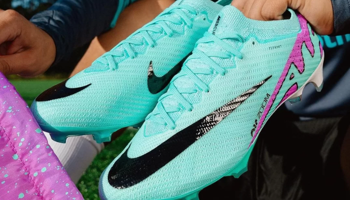 chuteira Nike Zoom Mercurial Vapor 15 Elite FG Pack Peak Ready. A chuteira é predominantemente turquesa com detalhes em roxo e preto. Possui um design moderno e esportivo, com o Swoosh da Nike na lateral. A descrição detalha os benefícios da chuteira, incluindo a unidade Zoom Air para impulsos extras, o cabedal Vaporposite+ para controle de bola e os studs tri-estrela para tração multidirecional.