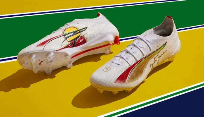 Chuteira Puma Ultra 5 Ultimate FG Senna nas cores branca, vermelha, dourada e verde, projetada para homenagear Ayrton Senna, com tecnologia SPEEDSYSTEM para máxima aceleração, cravos FastTrax para tração superior e suporte PWRTAPE SQD para estabilidade e agilidade em campo.