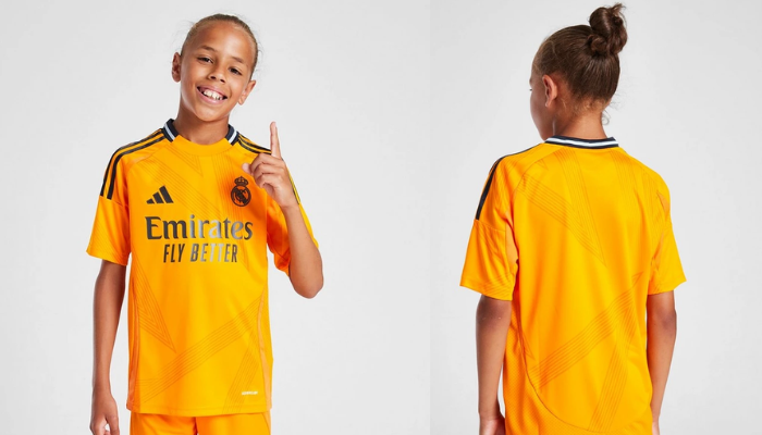 Conjunto Infantil Reserva Real Madrid Adidas 2024-2025 na cor laranja, branco e preto. A camisa possui gola redonda com nuca azul marinho e friso azul claro, três listras da Adidas nos ombros em azul marinho, escudo do Real Madrid e logo da Adidas aplicados em azul marinho, e patrocínios. O calção é na cor laranja e tem o escudo do Real Madrid aplicado na perna esquerda. 