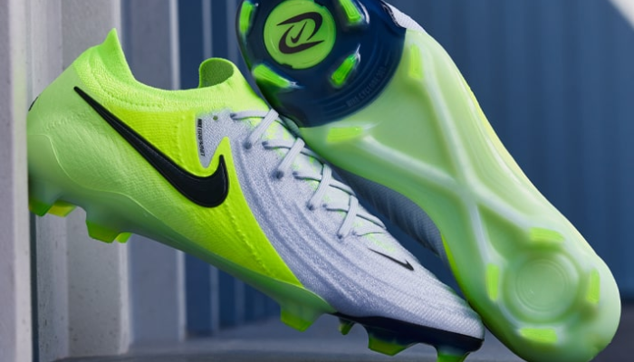 A chuteira Nike Phantom GX II Elite FG Mad Voltage, em cinza, verde fluorescente e preto, apresenta um design moderno e tecnológico. O cabedal é composto pelo material Gripknit, que proporciona um toque excepcional à bola