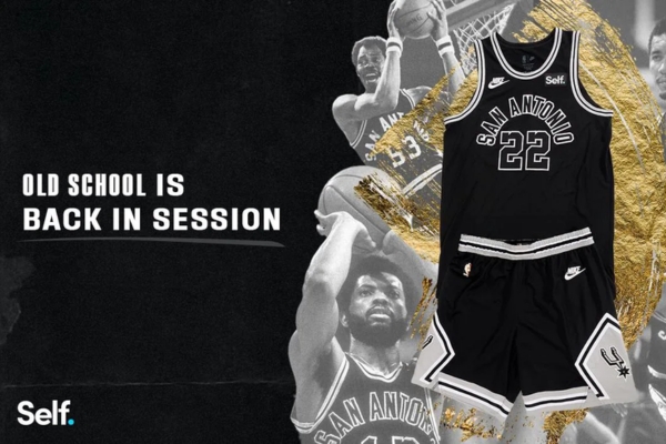 Regata Classic Edition do San Antonio Spurs Nike 2022/23, homenageando 50 anos de história. Uniforme preto sobre preto, marca 'San Antonio' em destaque, números dos jogadores costurados, detalhes nostálgicos. Celebre com estilo!