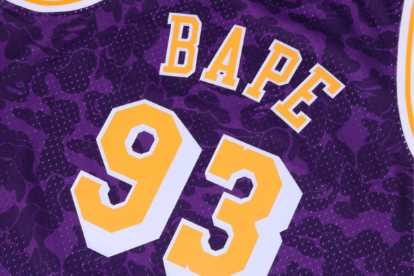 Regata Los Angeles Lakers BAPE X Mitchell & Ness nas cores roxa, amarela e branca. Design exclusivo com a icônica cabeça de macaco da BAPE e estampa camuflada. Uma fusão única de moda streetwear e esportividade da NBA | Tevo Sports