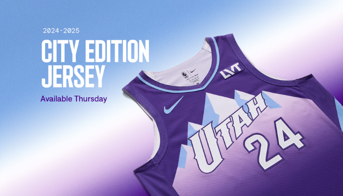 Regata Utah Jazz City Edition 2024-2025 da Nike. Design roxo com detalhes em branco e azul celeste, inspirado nas montanhas de Utah. Destaque para o logo "UTAH" moderno e a montanha estilizada no peito, além do logotipo "JAZZ" nas laterais.