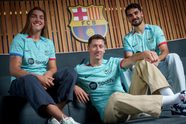 Terceira camisa Barcelona Nike 2023-2024 em verde água, detalhes azuis e vermelhos. Gola redonda com detalhes triangulares, escudo e Swoosh Nike em verde água. Punhos alternados azul e vermelho. Bandeira catalã na nuca, patrocínio beneficente UNHCR ACNUR em preto.