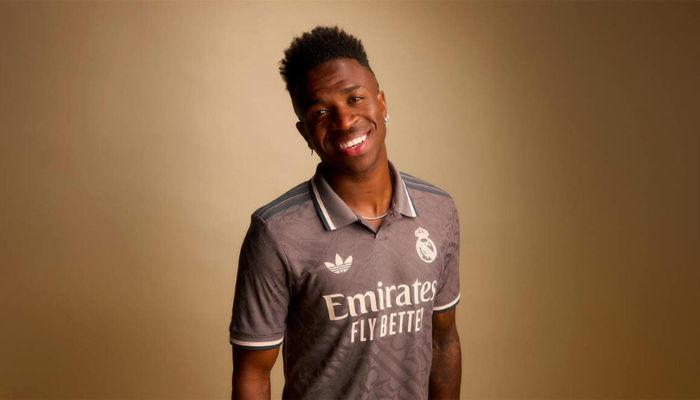 terceira camisa do Real Madrid para a temporada 2024/2025. A camisa é predominantemente cinza carvão com a sigla "RMCF" aplicada em jacquard ao longo de todo o corpo. A gola polo possui frisos em rosa e cinza escuro, assim como os punhos. O escudo do Real Madrid, em rosa, está localizado no lado esquerdo do peito, enquanto o logo da Adidas com o trefoil, também em rosa, está no lado direito.