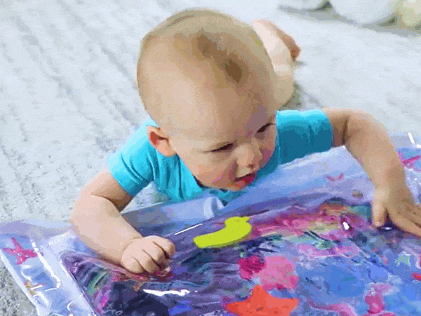Bebé alegre sorprendido yace boca abajo sobre una alfombra de colores en el  suelo