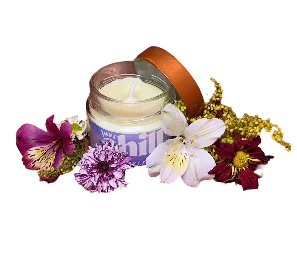 A imagem mostra uma vela aromática em um pote de vidro transparente, com um rótulo lilás onde está escrito "just chill". A vela está posicionada sobre um tecido acetinado na cor rosa, que serve de fundo, criando um ambiente elegante e acolhedor. Ao redor da vela, há várias flores em tons de branco, roxo e bordô, que complementam a composição com um toque natural e delicado. A luz suave ilumina a cena, destacando a textura do tecido e os detalhes das flores, tornando a imagem visualmente atraente e harmoniosa.