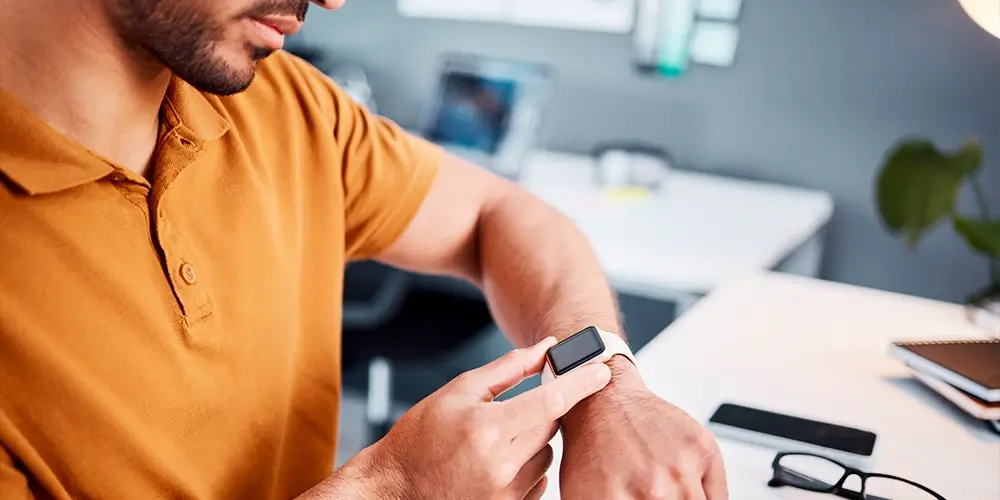 Homem em seu local de trabalho, consultando o planejamento do dia na tela de seu smartwatch