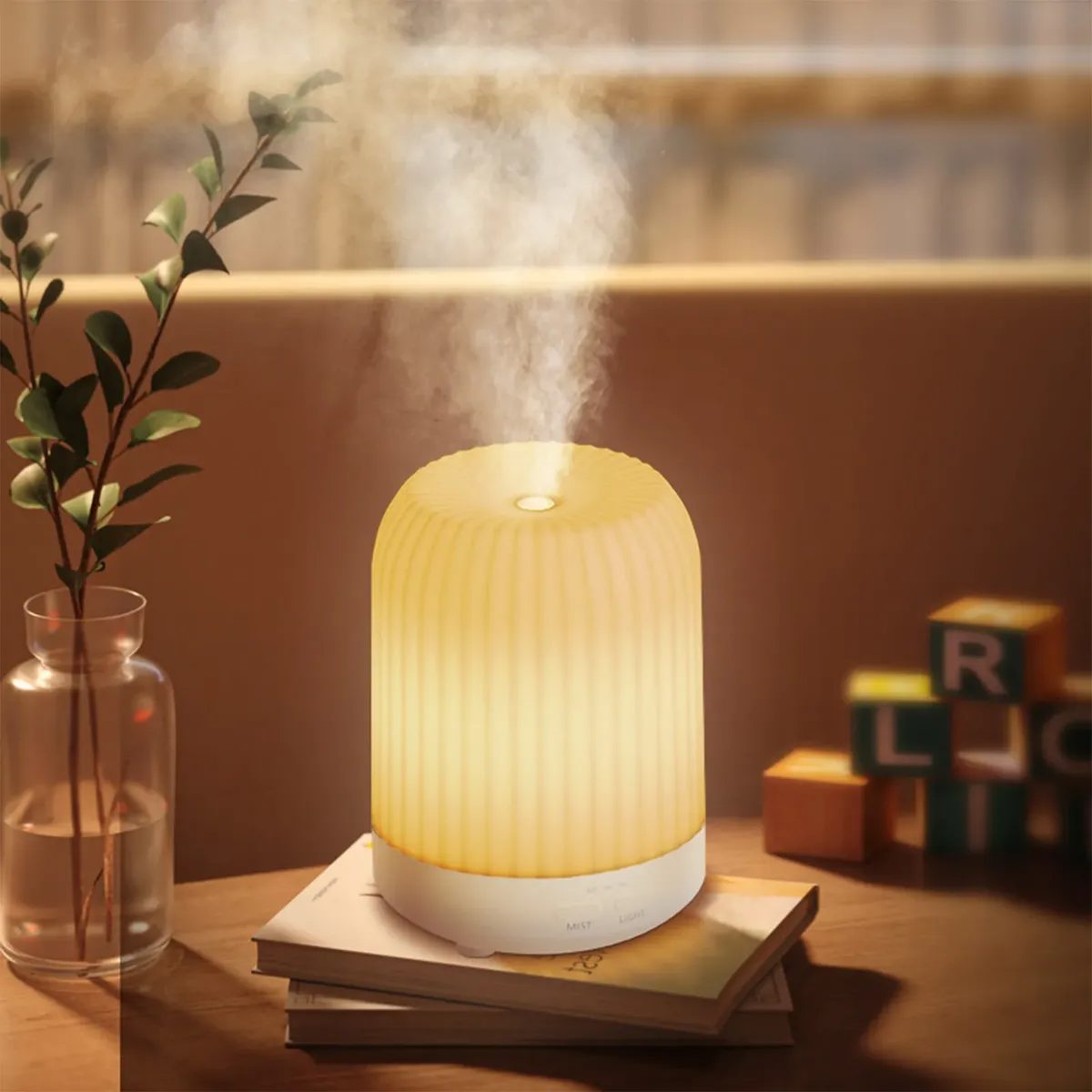 Home Difusor Eléctrico Make a Wish con luz cálida y niebla suave sobre una mesa con libros