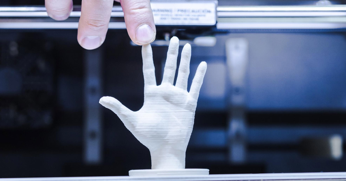 close em uma mão humana tocando uma miniatura de mão humana impressa em 3D